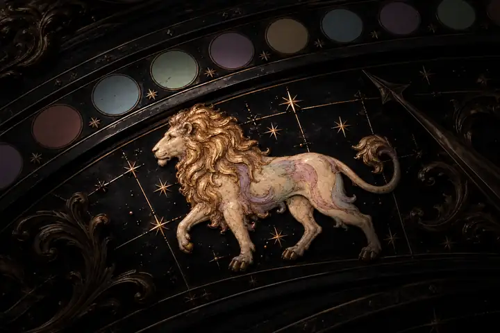 Illustrated lion with a golden mane in side profile, standing on an ornate bronze and black zodiac dial